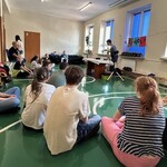 Uczniowie siedzą na podłodze w czasie apelu