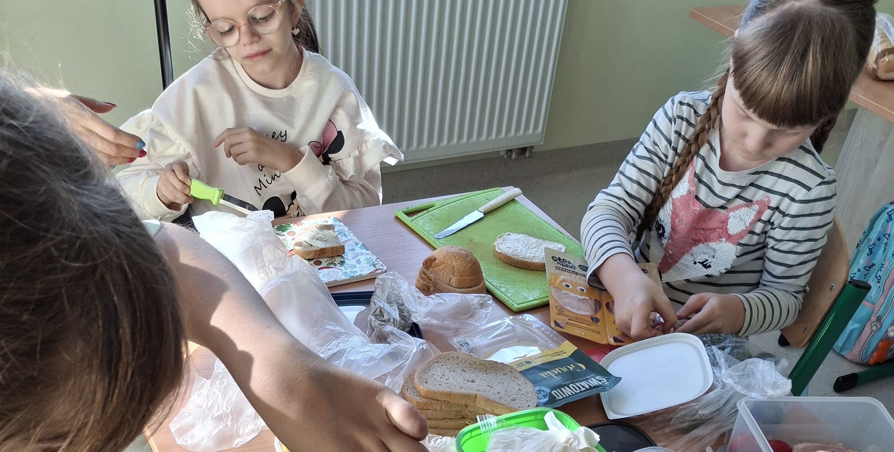 Uczennice siedzą wokół stołu i przygotowują kanapki