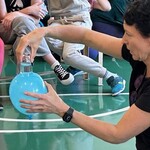 Nauczycielka demonstruje eksperyment trzymając w ręku balon, na balonie szklanka z wodą