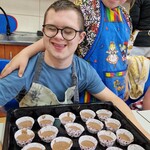 Uczeń siedzi przy stole i trzyma przed sobą blachę z babeczkami.