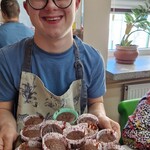 Uczeń trzyma przed sobą talerz upieczonych babeczek.