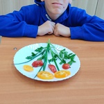 Uczeń siedzi przy stole. Przed nim stoi talerz z ułożonym bukietem z pomidorów.