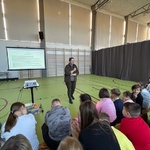 Pani leśniczy mówi przez mikrofon stojąc przed uczniami