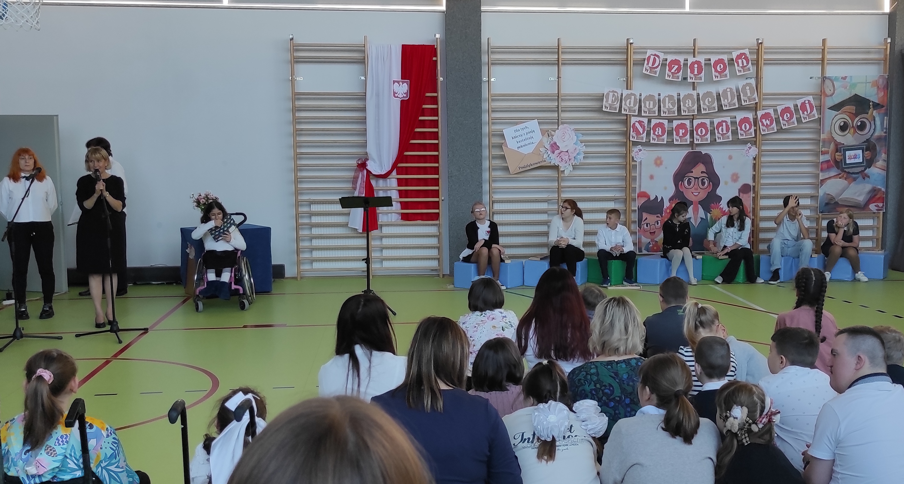 Pani dyrektor mówi do społeczności szkolnej zgromadzonej na sali gimnastycznej