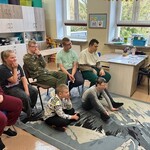 Uczniowie siedzą na krzesłach, albo na podłodze, patrzą w jednym kierunku
