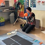 Nauczyciel dmucha balon, przed nim leżą cztery czarne kartki