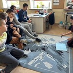 Uczniowie siedzą, nauczyciel na podłodze rysuje plan zajęć.
