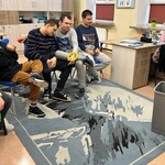 Nauczyciel wyjmuje coś z wiaderka, uczniowie patrzą siedzą na krzesłach.