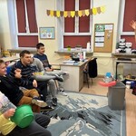 Uczniowie siedzą na krzesłach i patrzą na nauczyciela.