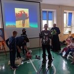 Uczennica z nałożonymi na nogi nartami. Obok stoi ksiądz i koledzy