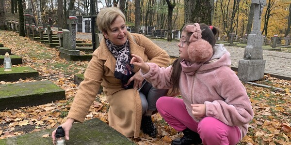Nauczycielka i uczennica stawiają znicz na grobie.