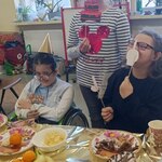 Jubilatka stoi, jej koleżanki siedzą przed urodzinowym stołem