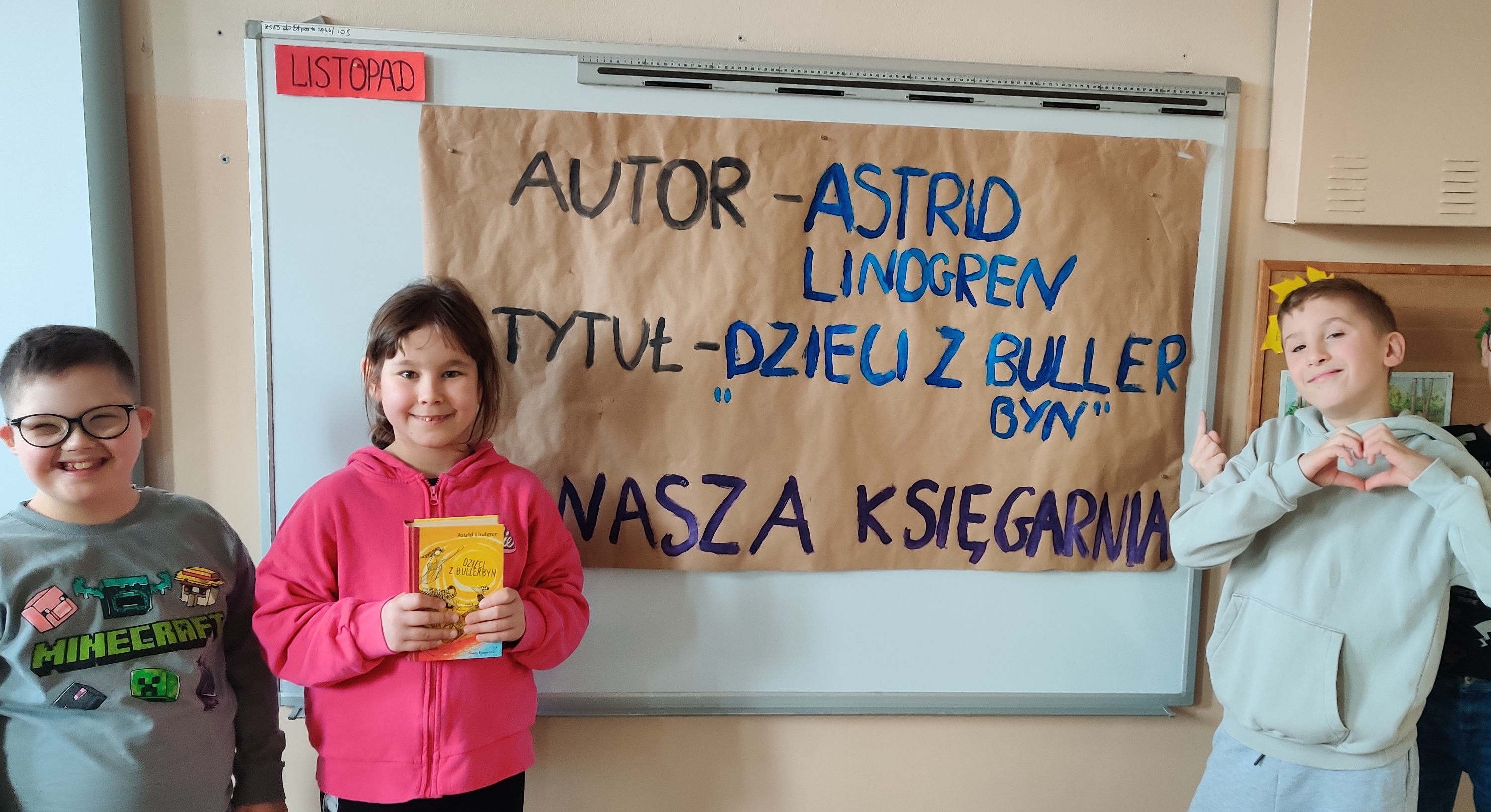 Uczniowie pozują na tle arkusza papieru z napisem autora i tytułem omawianej książki