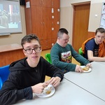 Uczniowie siedzą przy stole i jedzą szarlotkę