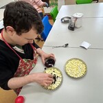 Uczeń wkłada żurawinę na pokrojone jabłka do małej tartaletki