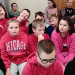 Uczniowie  w czerwonych ubraniach siedzą na ławkach