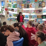 Nauczycielka mówi do uczniów siedzących na ławeczkach