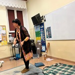 Nauczycielka stoi w pracowni i pokazuje symbol