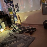 Nauczycielka leży przykryta kocem na podłodze w pracowni i wyciąga rękę w kierunku włączonej lampki