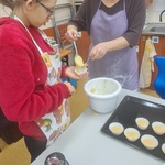 Nauczycielka pomaga uczennicy wkładać ciasto z miski do foremki