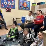 Uczniowie siedzą na krzesłach i na podłodze w klasie