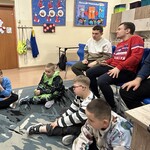 Uczniowie siedzą na krzesłach i na podłodze w klasie