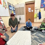 Uczniowie siedzą na podłodze i patrzą na nauczyciela