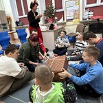 Uczniowie siedzą na dywanie, podają sobie prezent