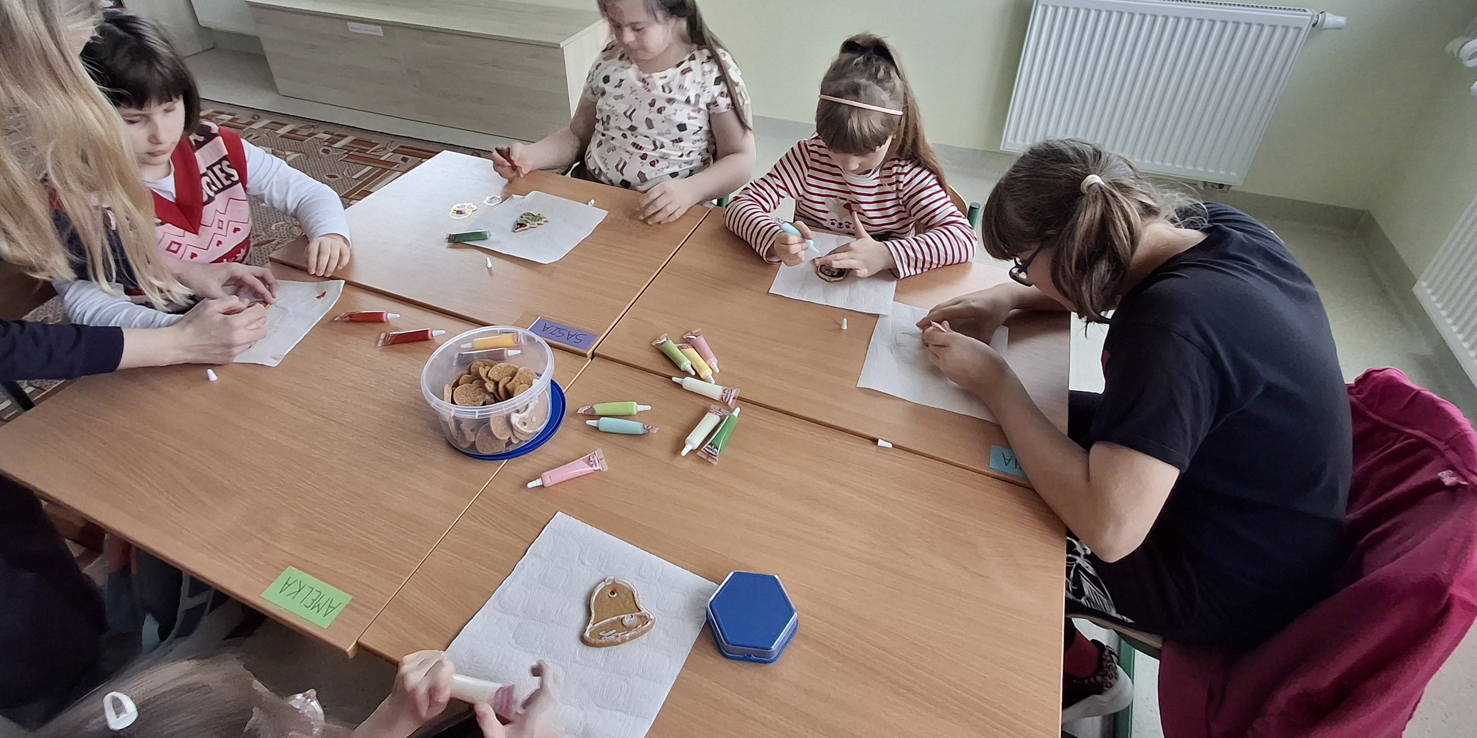 Uczennice siedzą przy stolikach i dekorują pierniki