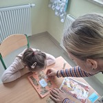 Uczennica pracuje przy stoliku z pomocą nauczyciela