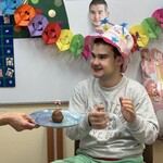 Jubilat siedzi w urodzinowej czapce na honorowym miejscu