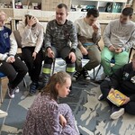 Uczniowie siedzą na podłodze i na krześle