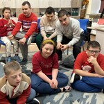 Uczniowie siedzą na podłodze i na krzesłach.