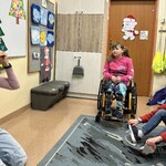 Uczniowie siedzą na podłodze i na krzesłach. Nauczyciel jest w kapeluszu