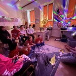 W pomieszczeniu jest ciemno, świecą się kolorowe lampki. Uczniowie siedzą na podłodze i na krzesłach.