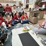 Uczniowie siedzą na podłodze i na krzesłach.