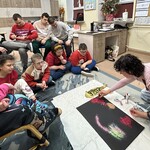 Uczniowie siedzą na podłodze i na krzesłach. Nauczyciel sypie brokat na kartkę.