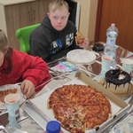 Uczniowie siedzą przy stole i jedzą pizzę