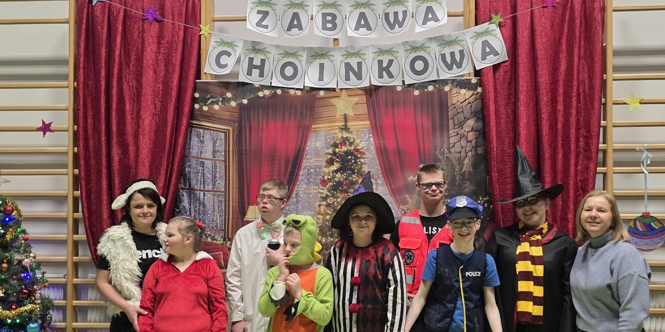 Nauczycielka, pomoc i uczniowie w strojach karnawałowych na tle dekoracji