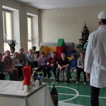 Uczestnicy półkolonii zimowych siedzą na ławeczkach  i patrzą na naukowca w białym fartuchu i kasku na głowie