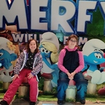 Dwie dziewczynki na tle ścianki z reklamą filmu Smerfy