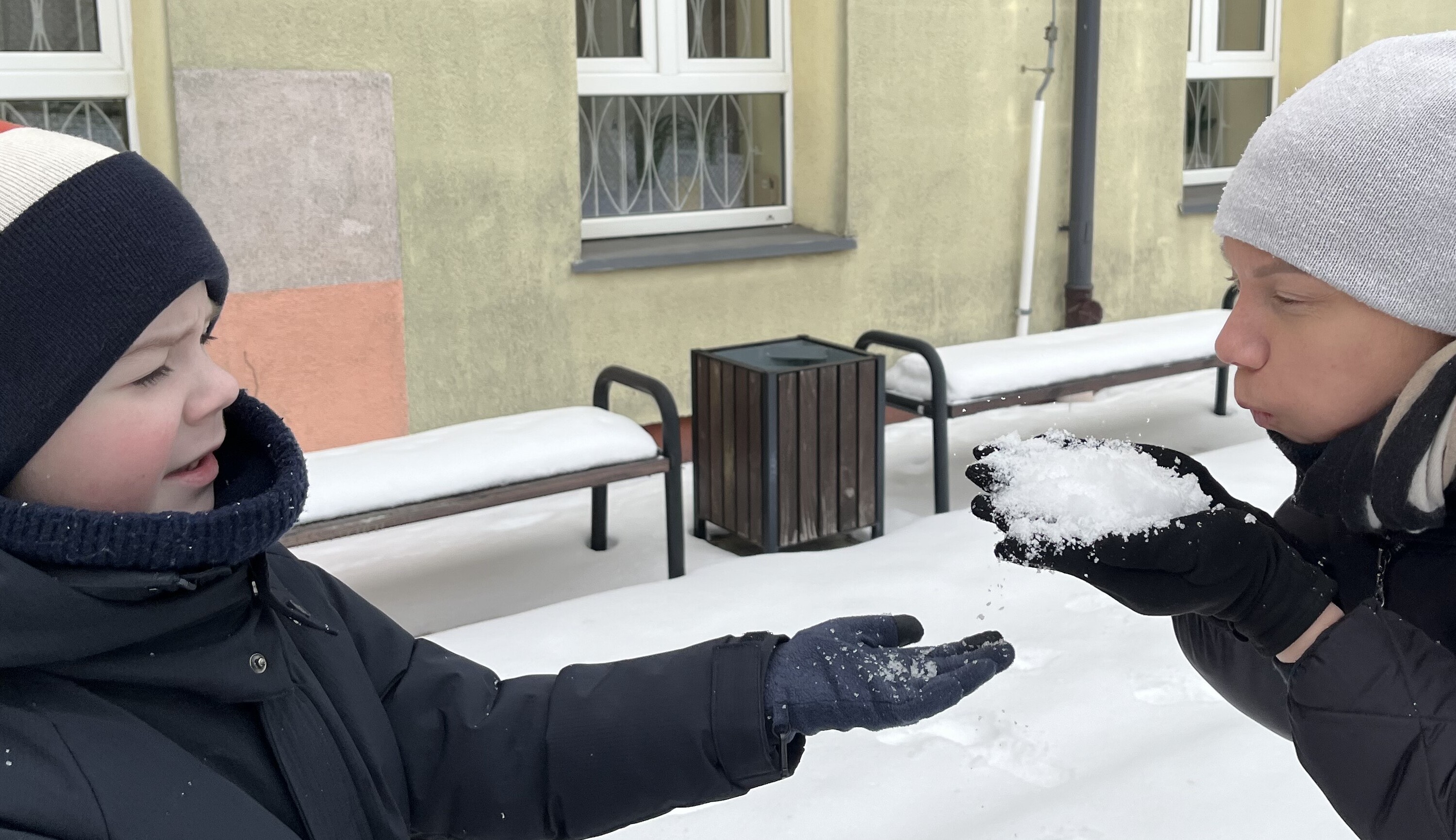 Nauczycielka dmucha na śnieg trzymany w ręce w stronę ucznia