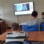 Uczniowskie siedzą w ławkach i patrzą na wyświetlany slajd na ekranie