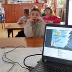 Uczniowskie siedzą w ławkach i patrzą na wyświetlany slajd na ekranie