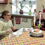 Na stole stoi tort z palącymi się racami. Wokół stołu siedzą uczniowie