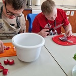 Uczniowie siedzą przy stole i kroją warzywa