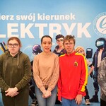 Uczniowie pozuje na tle plakatu reklamującego szkołę ponadpodstawową