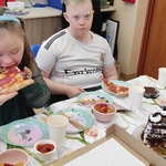 Uczniowie siedzą przy urodzinowym stole i jedzą pizzę