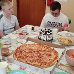 Uczniowie siedzą przy stole na którym stoi pizza i tort