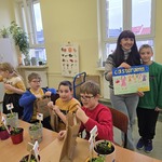 Uczniowie w trakcie warsztatów sadzenia kwiatów. Z tyłu uczeń i Pani z pracą plastyczna